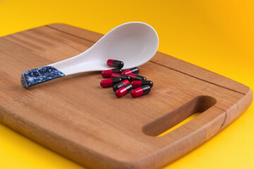 Pharmaceutical medicine pills spilled from porcelain spoon placed on a chopping board with isolated yellow background