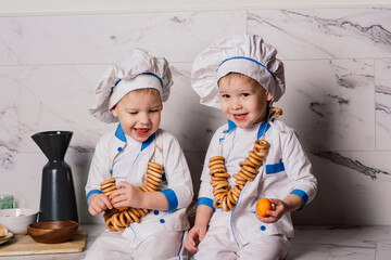 Little cute cook with cutlery sitting on a kitchen, twin brothers, tangerine, bagels