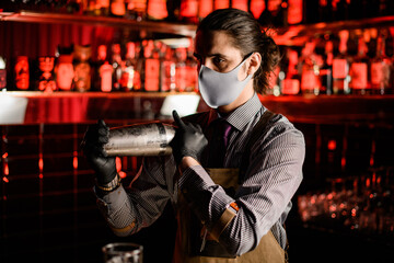 side view of man bartender in apron and mask and gloves with steel shaker