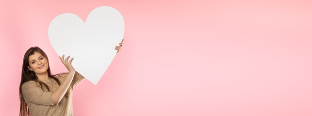Girl with a large white heart shape in the hands. A student in love stands and holds a large heart shape in her hands. Valentine's Day and love. Panoramic frame.