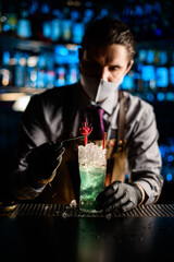 young male bartender decorates with flower a glass of cold blue cocktail