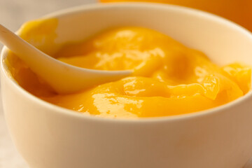 Lemon curd in a sausepan white bowl.Close-up yellow smooth background.Horizontal