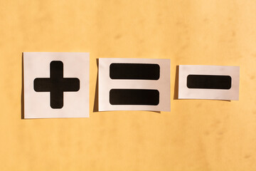 Symbols of black color plus, minus and equals on beige background. Abstraction