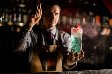 man bartender holds glass with cold cocktail decorated with flower and sprinkles on it