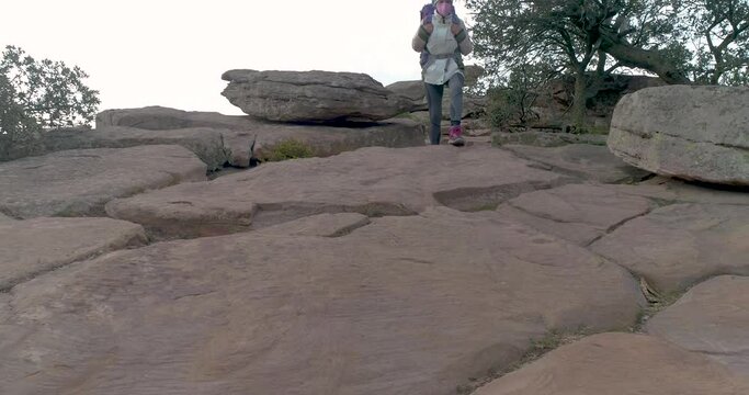 ras de suelo de mujer adulta caminando por ladera rocosa con macuto