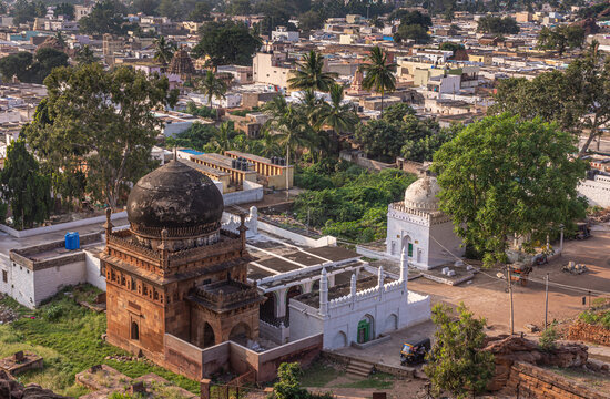 Badami, Karnataka, India - November 7, 2013: Aerial view on red sonte Jamia Mashid or mosque blackened by mold dome in wide cityscape. Green foliage around.