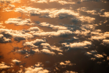 view of the clouds from above from the plane. the sea is colored by the setting sun.