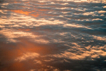 view of the clouds from above from the plane. the sea is colored by the setting sun.