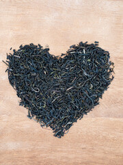 dry green tea with jasmine petals laid out on a wooden table in the form of a heart