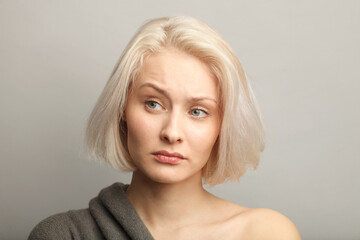 middle aged blonde woman moving brow skeptically looking aside, isolated on gray background