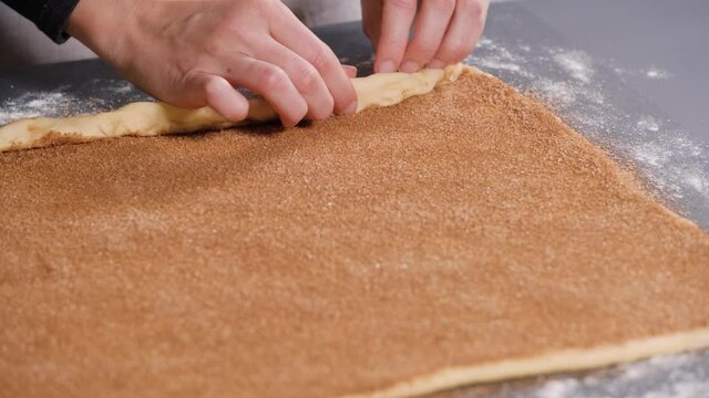 Woman rolling out dough for buns with cinnamon