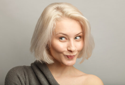 close up attractive blond hair woman with cunning smirk, constrain laugh, isolated on gray background