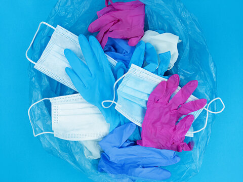 Medical pandemic coronavirus waste, face masks and latex gloves in garbage bag on blue background.