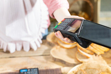 The shop assistant accepts payment via the mobile phone for the sold bread. Cashless payment in the bakery store.