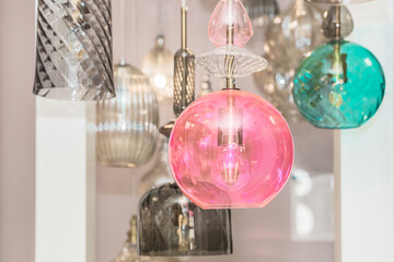 A group of switched-off multicolored lamps with a gray, turquoise, pink glass ceiling is suspended in the white interior. Concept of hotel decoration. Indoors. Close up.