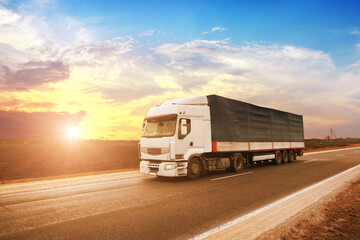 Obraz na płótnie Canvas A big truck with a trailer on a road against a sky with a sunset