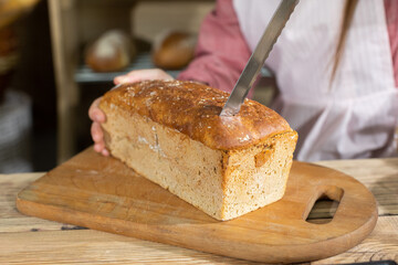 A new and young saleswoman in a bakery shop is slicing bread from a mold. For the first time in a...