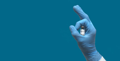 Hand in  medical glove holds syringe and bottle with vaccine for COVID-19 showing OK sign as...