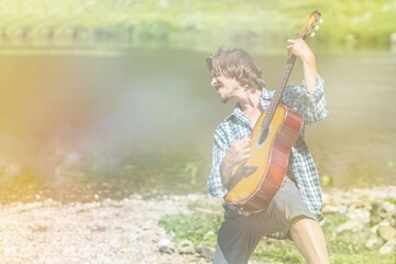 Musician male in an open shirt enthusiastically plays the old guitar in nature. Summer, clear day....
