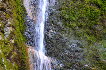 Small waterfall on a rocky stream stone background. Mountain covered with green moss. Concept for refreshing coolness or clear water