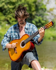 Rock musician man in an open shirt enthusiastically plays the old guitar in nature. Summer, clear day. Retro style. Musical concept. Portrait, close-up. Instagram size photo.