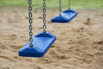 Two empty blue plastic swings for children hang from metal chains in a playground during the lockdown in the coronavirus pandemic, copy space