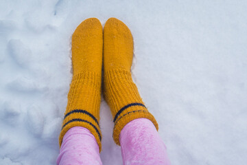Female legs in warm pink pants and yellow socks on a snow background outdoors