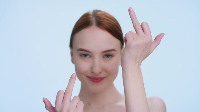 Close-up beauty portrait of young redhead woman on light blue background making a middle finger gesture at the camera
