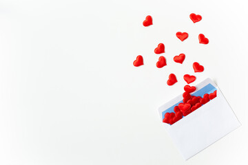 
White postal envelope with flying red decorative hearts is located on a white background. Valentine's Day theme. Free space for text.