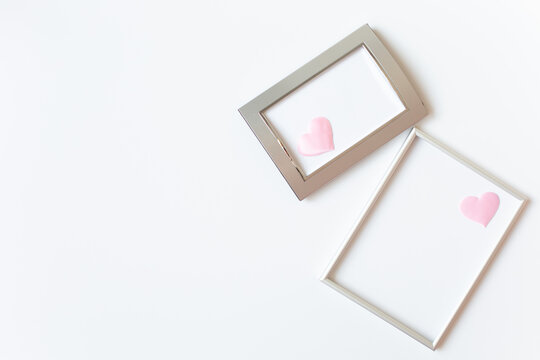 Two silver photo frames decorated with pink hearts with space for outside text are on a white background on the right side of the image. Valentine's Day theme. Copy space.