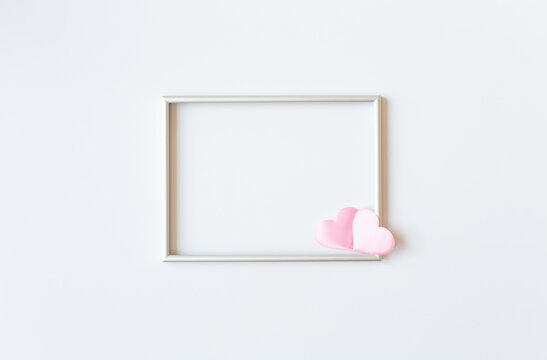 A silver photo frame decorated with two pink satin hearts is on a white background in the middle of the image. Valentine's Day theme. Free space for text.