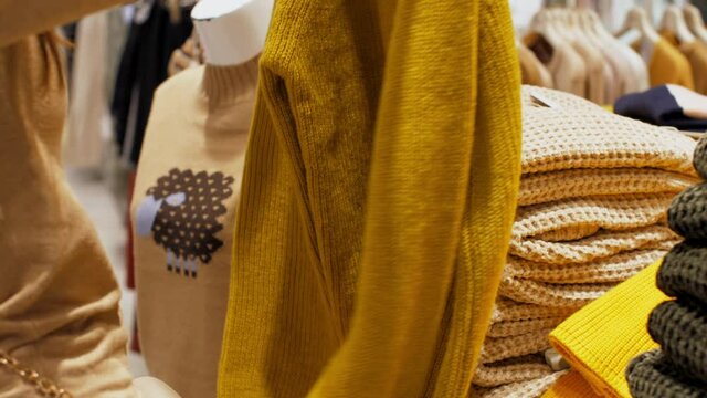 Professional shopper holds yellow woollen pullover in hands and puts on department store shelf. Concept sales and discounts
