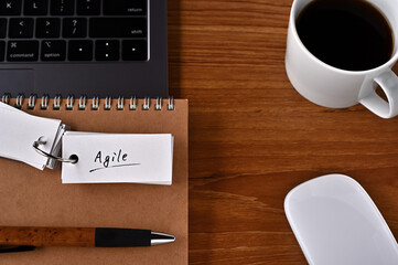 On the desk there is a laptop, a cup of coffee, and a word book with the word agile written on it. It was an abbreviation for agile software development.