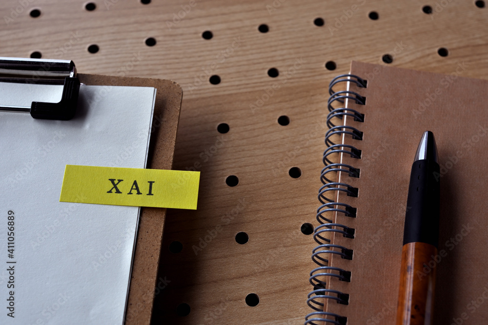Poster there is a notebook, a pen, and a clipboard with a sticky note stuck to it that says xai written on 