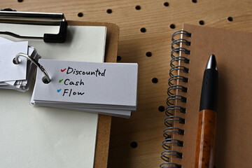 On the desk there is a clipboard, a notebook, and a word book with the word discounted cash flow.