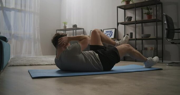 physical exercise on oblique abdominal muscles, man is training at home, lying on floor and doing crunches
