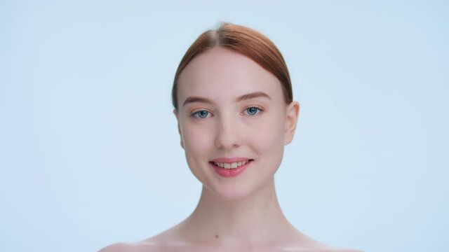 Young attractive ginger woman touches her face runs fingers from under her eyes up to her temples and down along her cheeks | Skincare products beauty portrait
