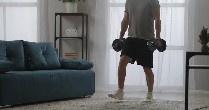 adult strong man is doing exercises with weight, squatting with dumbbells in hands, strength training in home gym