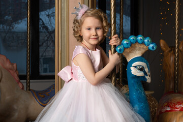a little girl in a pink dress and a crown on a carousel with a white hare