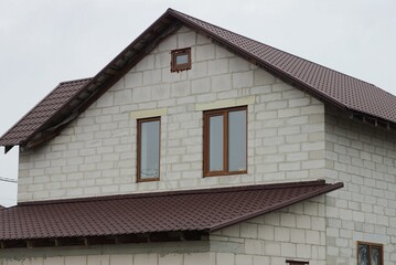 big attic of a white brick house with windows under a brown tiled roof against a gray sky