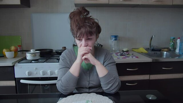 sad woman sitting in the kitchen, worried and thinking about something