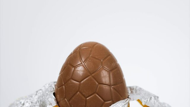 Stop motion footage of a milk chocolate Easter egg wrapped in gold foil being slowly unwrapped and eaten bite by bite until there is nothing left. White background with copy space available
