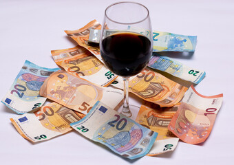 glass of wine with a lot of money on the floor, euro notes of five, fifty, twenty and ten.