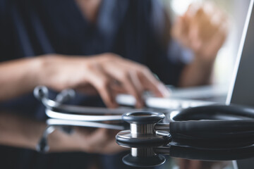 Doctor working on laptop computer in medical office with medical stethoscope on table, medical background