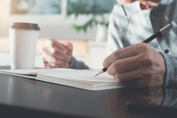 Casual man hand with a pencil writing on paper notebook on wooden table during working from home