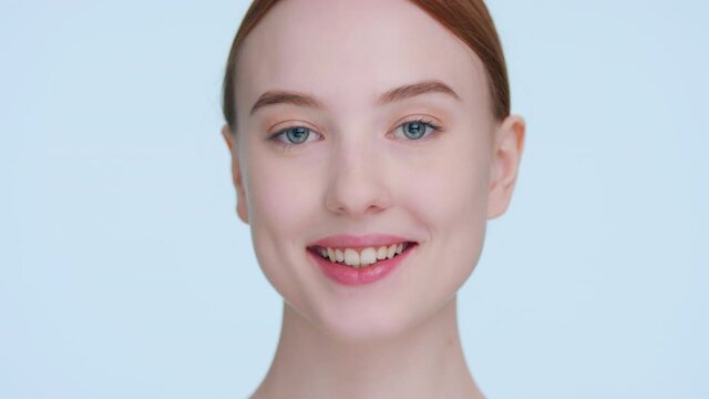 Extreme close-up beauty portrait of young ginger woman who touches her elastic face skin, looks at camera and smiles