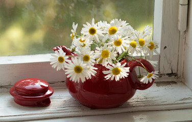 A bouquet of daisies in a red vase on a white wooden window.