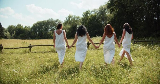  Four girls walk across the lawn in white transparent dresses