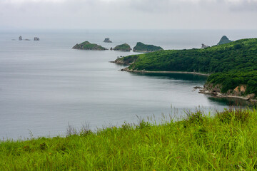 Bay of the sea from the top of a hill of a mountainous coast with an island in the background, summer landscape and seascape in cloudy cloudy weather.