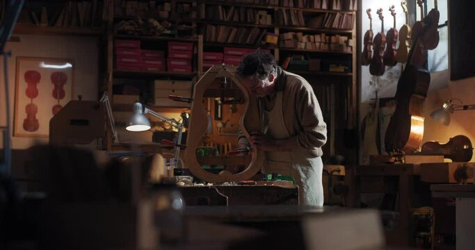 Cinematic shot of master artisan luthier working on creation of handmade fine quality wood violin in creative workshop. Concept of spiritual instrument, handmade, art, orchestra, artisan, music.